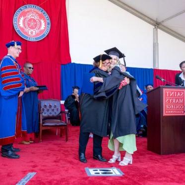 A graduate hugging an administrator on stage